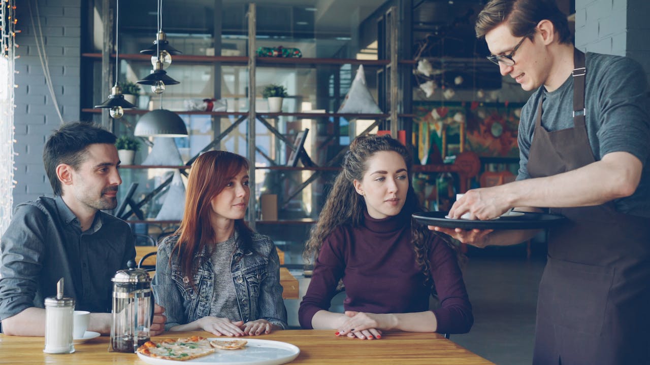 Friendly waiter serving food to young adults in a stylish cafe setting.