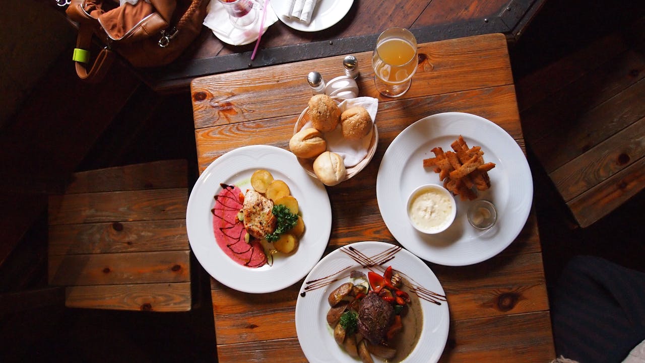 Aerial view of a rustic wooden table set with gourmet dishes, bread, and a drink, creating a warm dining atmosphere.